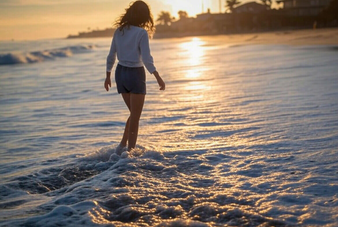 Escena de vida junto al mar con una persona caminando en la playa y casas modernas al fondo, transmitiendo bienestar, exclusividad y estilo de vida relajado.